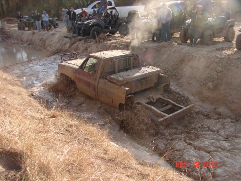 1987 Ford Bronco - A pickup truck struggles through a muddy obstacle course, surrounded by onlookers and other off-road vehicles.