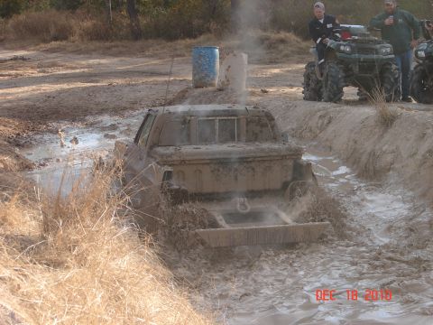 1987 Ford Bronco - Pickup truck stuck in mud pit with ATVs nearby.
