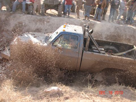 1987 Ford Bronco - A blue pickup truck is stuck in a muddy ditch, with spectators watching from above.