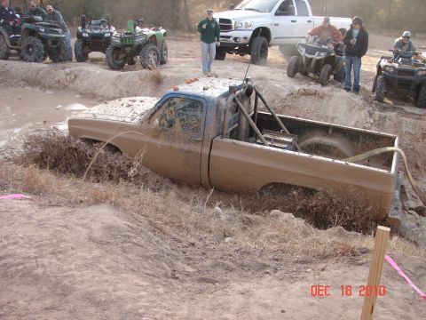 1987 Ford Bronco - A muddy pickup truck is stuck in a mud pit while other vehicles and people watch.