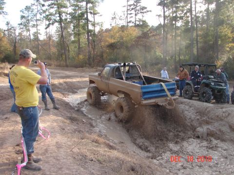 1987 Ford Bronco - A lifted pickup truck navigates a muddy off-road course with spectators watching.