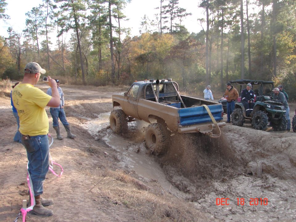Brown pickup truck with blue bed sides driving through mud, lifted with large tires
