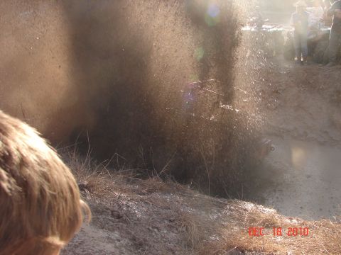 1987 Ford Bronco - Vehicle powers through a muddy obstacle, creating a large spray.