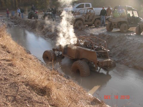 1987 Ford Bronco - Multiple off-road vehicles navigate a muddy track, with one buggy stuck and steaming.