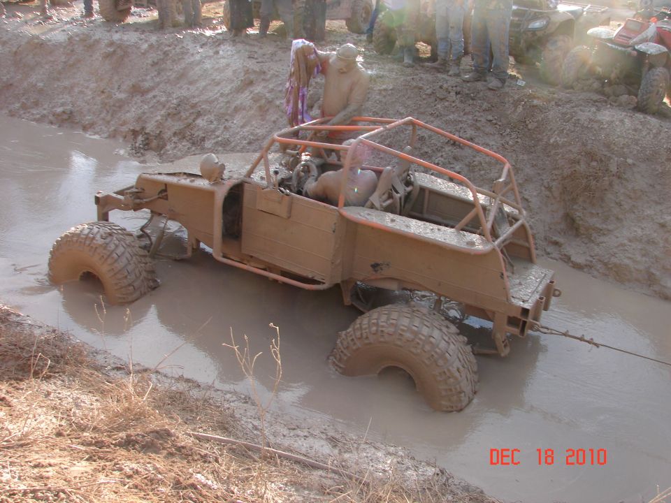 Muddy off-road buggy with roll cage stuck in a muddy ditch, people watching