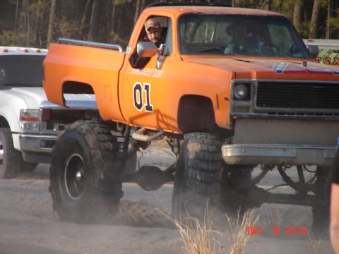 1987 Ford Bronco - An orange pickup truck, modified with a lift kit and oversized tires, is seen on a sandy surface.