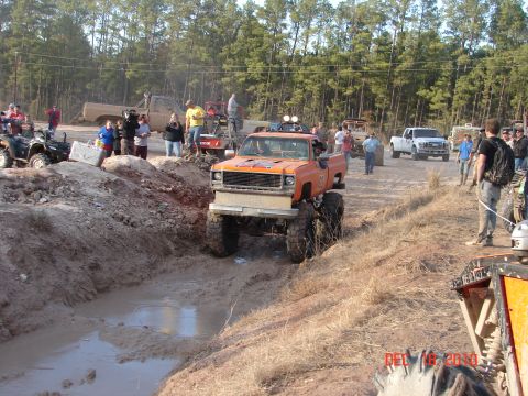 1987 Ford Bronco - Modified pickup truck navigates a muddy obstacle course with spectators present.