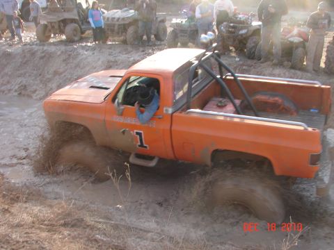1987 Ford Bronco - Pickup truck stuck in mud during an off-road event with other vehicles and spectators present.