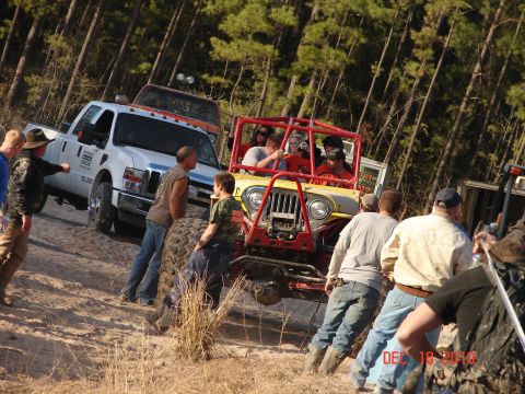 1987 Ford Bronco - A group of people gather around a yellow jeep with a red roll cage, possibly during an off-road event.