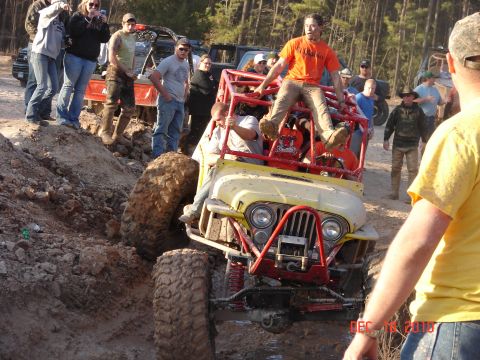 1987 Ford Bronco - Off-road enthusiasts watch as a modified jeep navigates a muddy obstacle.