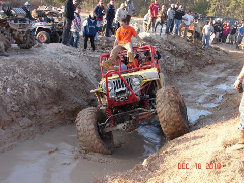 1987 Ford Bronco - A group of people watch as a modified Jeep navigates a muddy obstacle course.