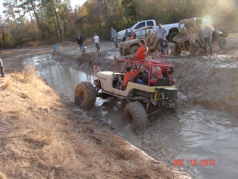 1987 Ford Bronco - This off-road vehicle, possibly modified, navigates a challenging mud pit with several other vehicles and spectators present.