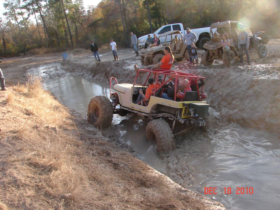 Off-road vehicle with red roll cage navigating a mud pit