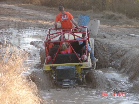 1987 Ford Bronco - People ride in a yellow off-road vehicle as it navigates a muddy track.