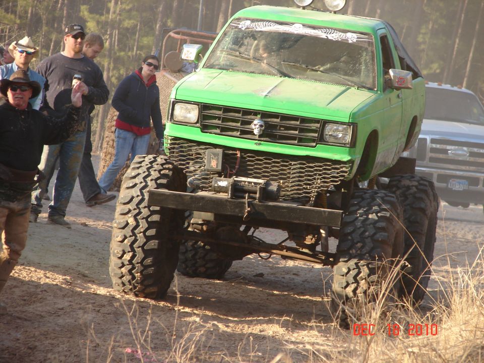 Green lifted pickup truck with large off-road tires and a skull on the grille, viewed from the front