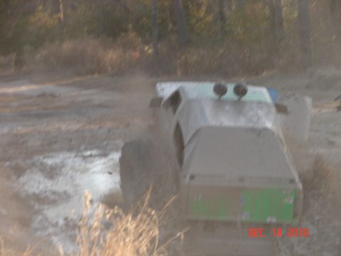 1987 Ford Bronco - This modified vehicle is seen driving through a muddy, outdoor area, kicking up dust.