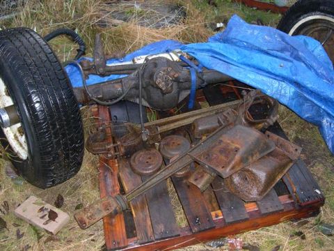 1982 Ford Bronco - Vehicle axle and brake components are piled on a pallet outdoors, covered partially by a blue tarp.