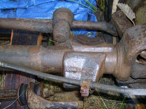 1982 Ford Bronco - Close-up of heavily rusted vehicle axle components, with a brake line running across the frame.