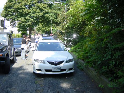 2003 Mazda 6 - A white Mazda 6 is parked on a street with trees and foliage. Another vehicle is visible to the left.
