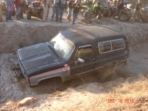 1987 Ford Bronco - This black SUV is stuck in a mud pit, with a crowd of people observing the scene.