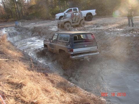 1987 Ford Bronco - Off-roading scene with a Chevrolet K5 Blazer stuck in mud, while other vehicles wait behind.