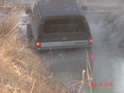 1987 Ford Bronco - A Chevrolet pickup truck with a camper shell navigates through a wet, muddy terrain.
