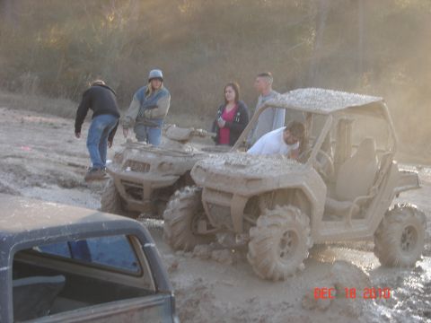 1987 Ford Bronco - Several people are gathered around muddy side-by-side ATVs stuck in a muddy field.