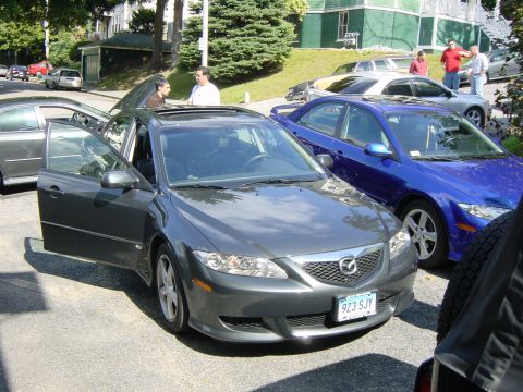 2003 Mazda 6 - A dark gray 2003 Mazda 6 sedan is parked on a street with its driver's door open, alongside a blue Mazda 6.