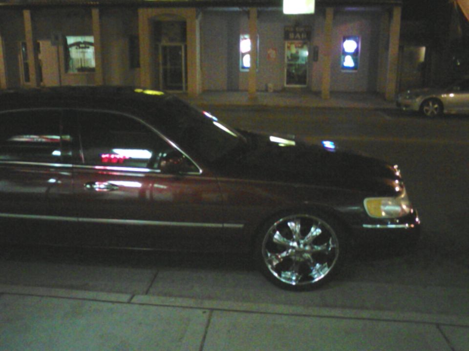 Dark 2000 Lincoln Town Car with chrome wheels parked at night