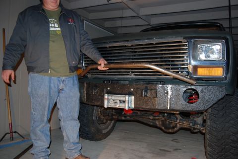 1982 Ford Bronco - A person holds a metal bar in front of a green Ford Bronco's grille and bumper.