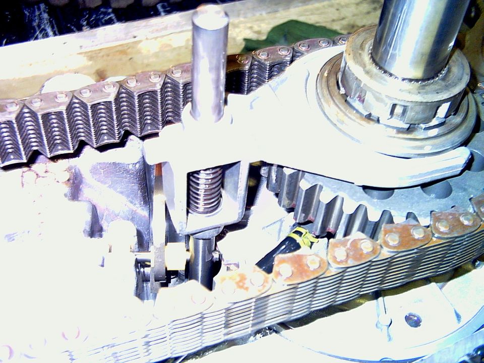 Close-up of a transfer case with a chain and gears. A metal arm with a spring is visible