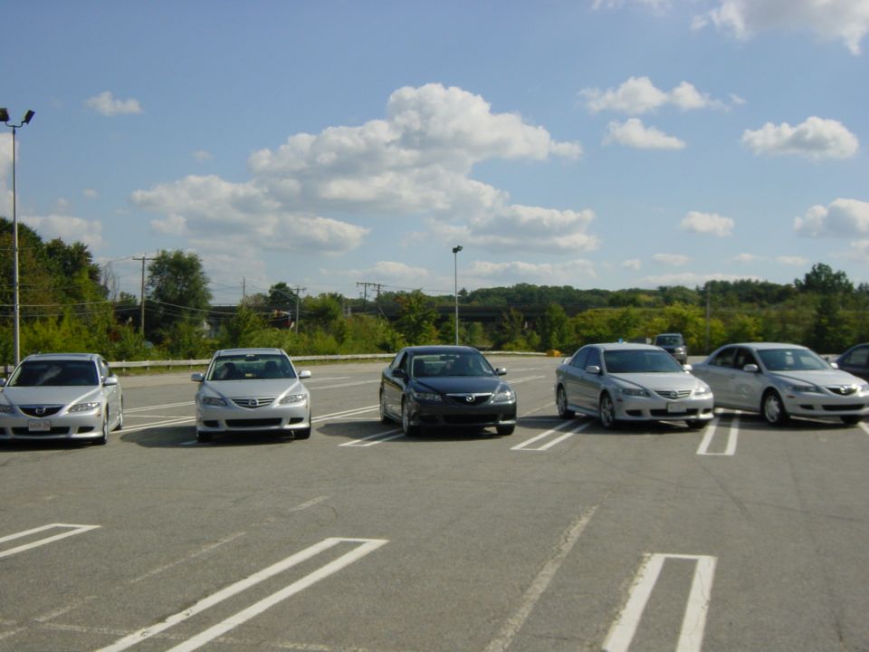 Row of five silver and dark sedans parked diagonally in a lot under a partly cloudy sky