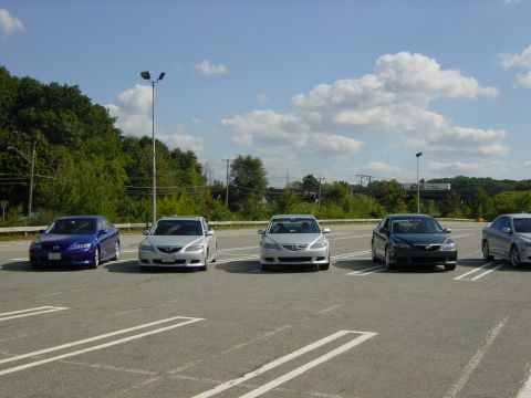 2003 Mazda 6 - A line of Mazda 6 sedans are parked in a lot under a bright, cloudy sky.