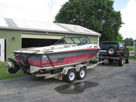 1995 Ford Bronco - A black SUV is hitched to a trailer carrying a red and white boat, parked in front of a green building.