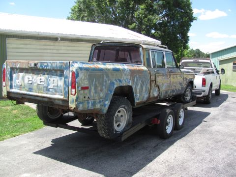 1986 Jeep Grand Wagoneer - A weathered Jeep pickup truck is loaded onto a trailer, with a white pickup truck following.