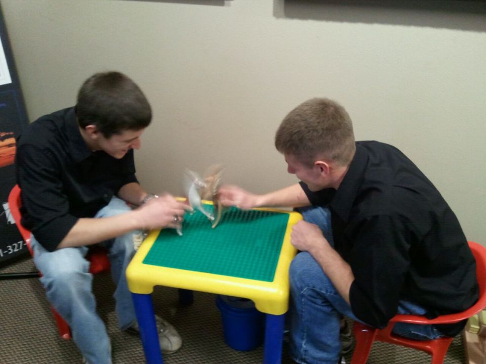 Two guys sit at a table playing with small toys