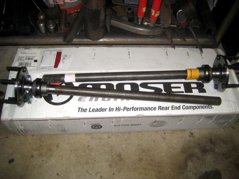 1996 Ford Bronco - Two Moser rear axle shafts are displayed on top of their product packaging in a workshop setting.