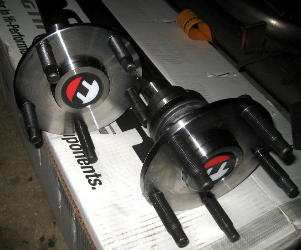 Two metal rear axle hubs with five studs each, resting on a cardboard box with text