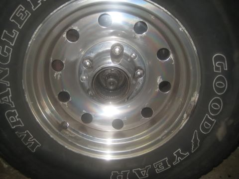 1990 Ford Bronco - Close-up of a polished aluminum eight-slot wheel mounted with a Goodyear Wrangler tire, showing the exposed hub and lug nuts at center. The…