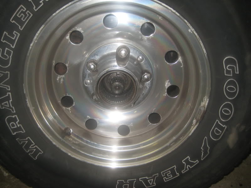 Polished 8-slot aluminum wheel with Goodyear Wrangler tire, close-up of hub and lugs