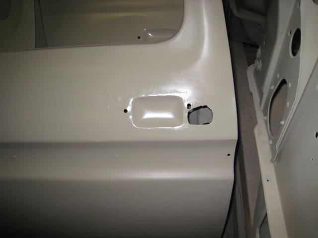 Close-up of a vehicle's interior door panel and frame, both primed for paint. Shows the door handle cutout