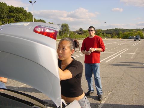 2003 Mazda 6 - A woman inspects the trunk of a silver 2003 Mazda 6, with a man standing in the background of a parking lot.