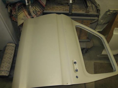 1976 Ford F-250 - A single vehicle door, primed and ready for paint, sits in a cluttered garage.