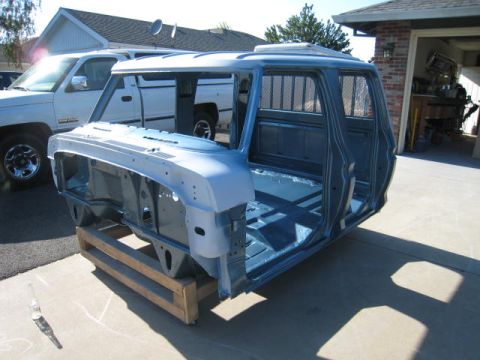 1976 Ford F-250 - A bare truck cab sits on a pallet in front of a garage, with a white pickup truck parked behind it.