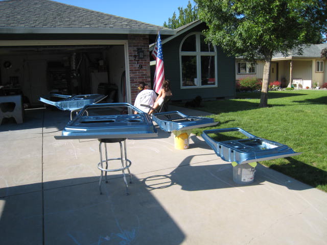 Four blue car doors laid out on a driveway, some on buckets, with a garage and house in the background