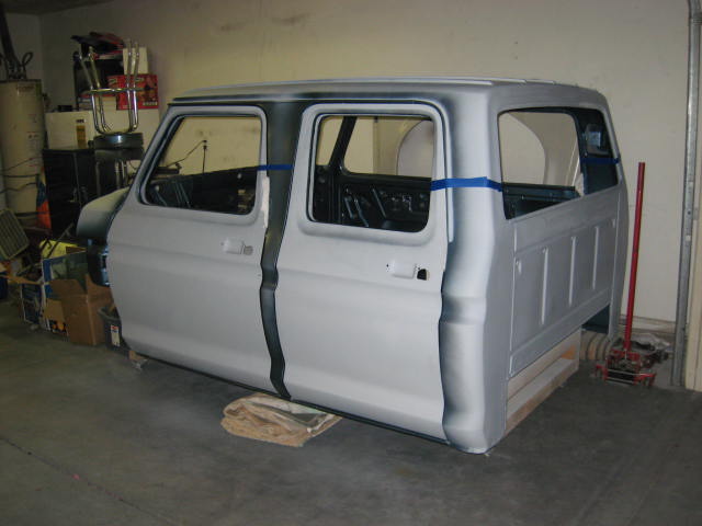 1973 Ford F-250 crew cab body shell in primer, sitting on blocks in a garage