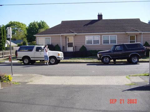 1979 Ford Bronco - Two Ford Broncos, one white and one black, are parked on a residential street.