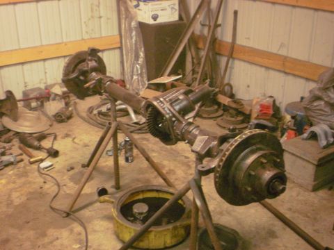 1995 Ford Bronco - A disassembled vehicle axle assembly is shown on stands, surrounded by various tools and spare parts in a workshop.