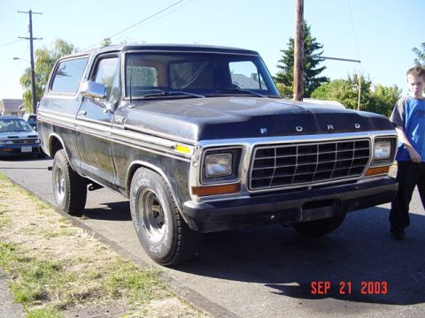 1979 Ford Bronco - A dark-colored Ford Bronco is parked curbside, with a young person standing nearby. The photo was taken in 2003.