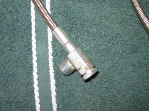 1992 Ford Bronco - A close-up view of a metal hose fitting with a T-junction, placed on a green fabric surface.